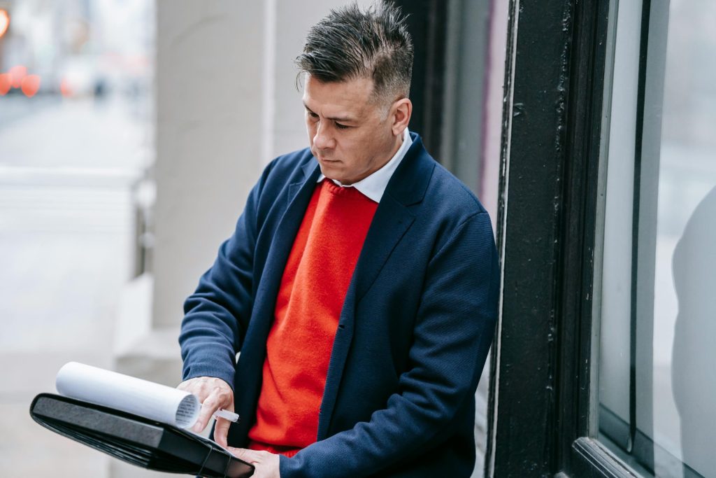 Professional man in a red sweater and suit reviewing paperwork outside during the day.